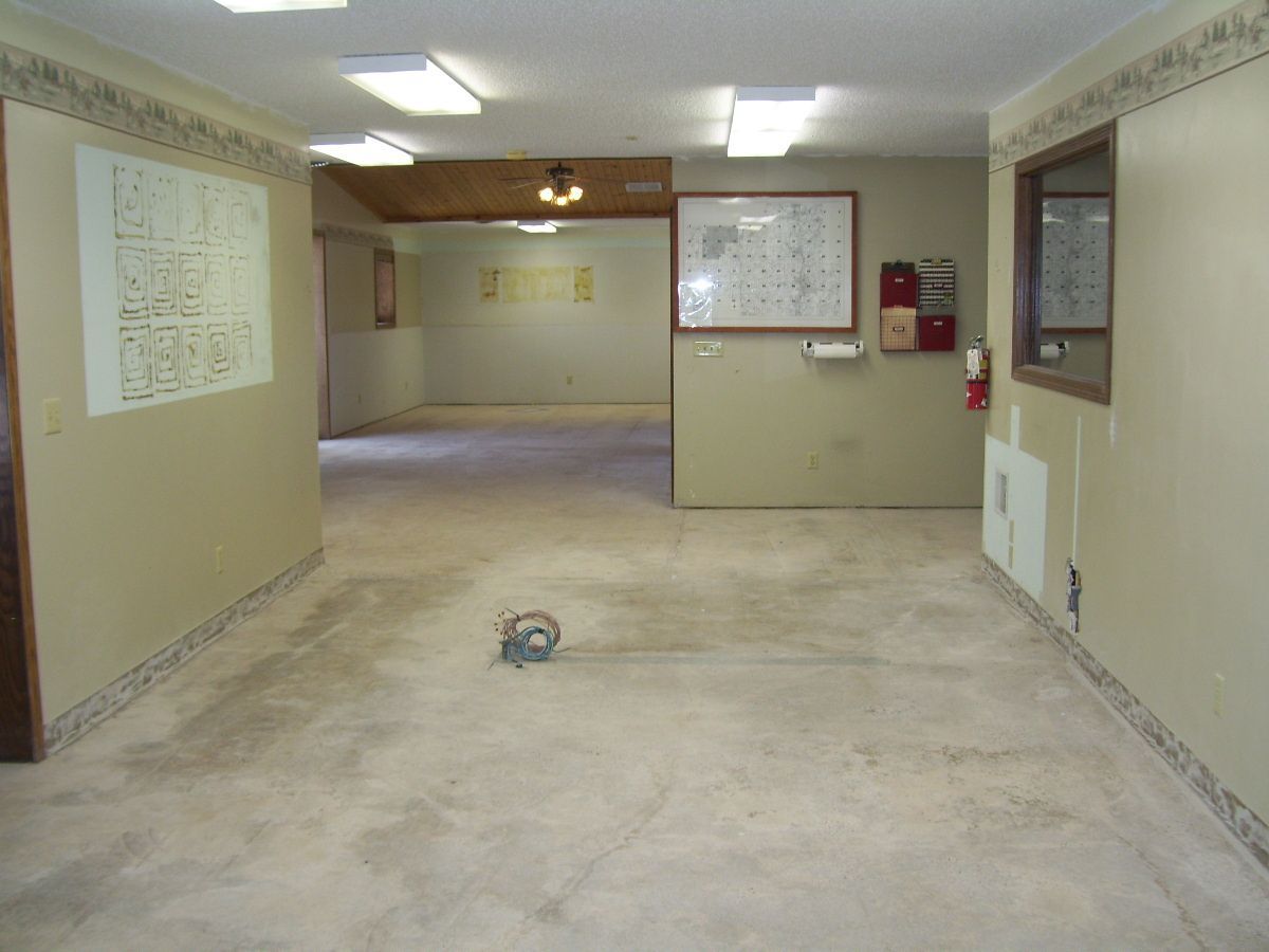Empty room with beige walls, fluorescent lights, and a rolled cable on the floor.