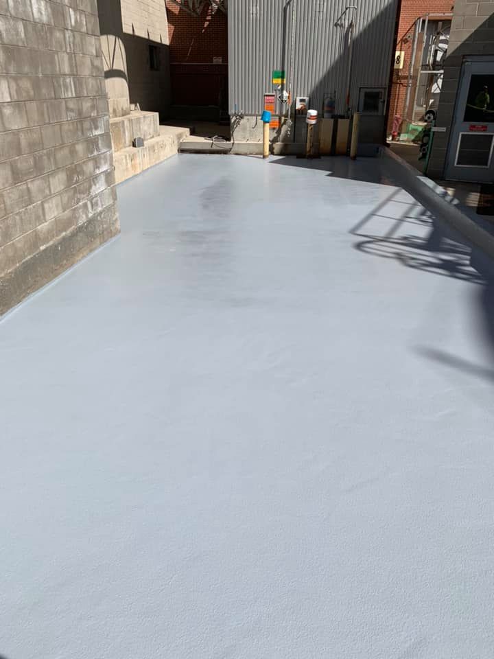 Newly painted light grey concrete surface in an outdoor alleyway, flanked by cinder block wall and building.