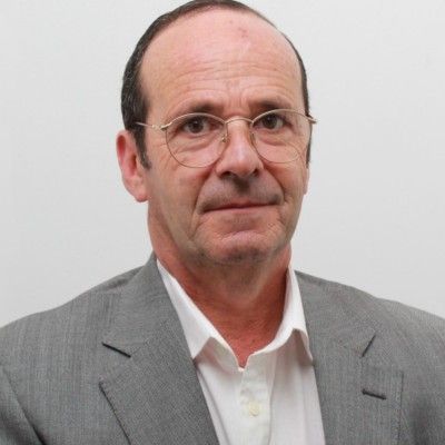 Um homem com barba está sorrindo e vestindo uma camisa azul.