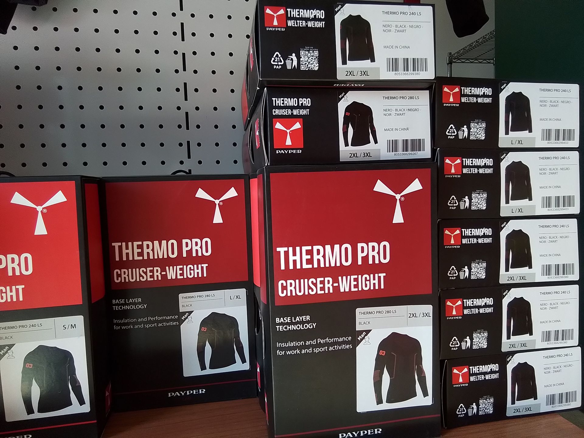 Scatole di abbigliamento Thermo Pro Cruiser-Weight impilate su uno scaffale. Colori rosso e nero con immagini dei prodotti.