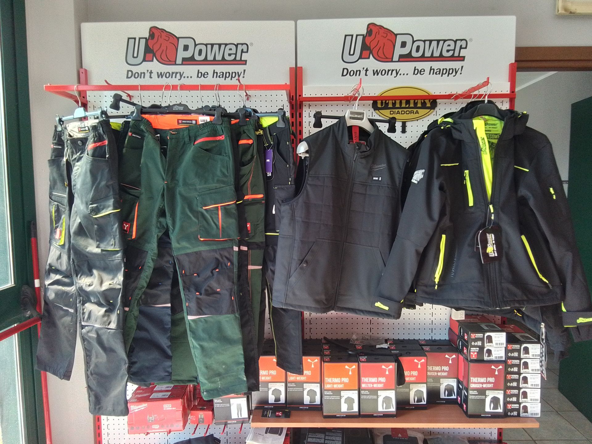 Esposizione di abiti da lavoro: pantaloni, giacche e stivali su uno scaffale con il marchio U-Power.