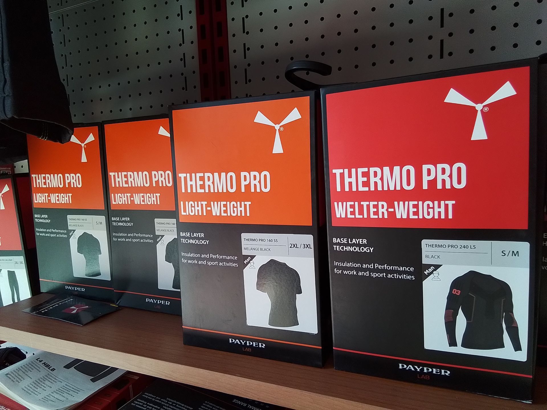 Scatole di magliette Thermo Pro, di varie grammature, sullo scaffale di un negozio. Confezioni arancioni e nere con illustrazioni di magliette.