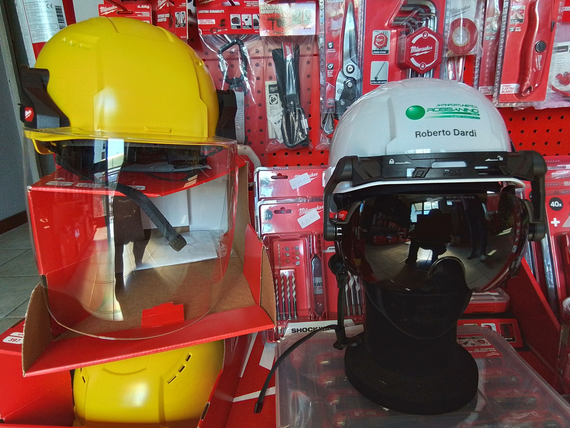 Due caschi di sicurezza con visiera esposti in un negozio: uno giallo e uno bianco con logo.