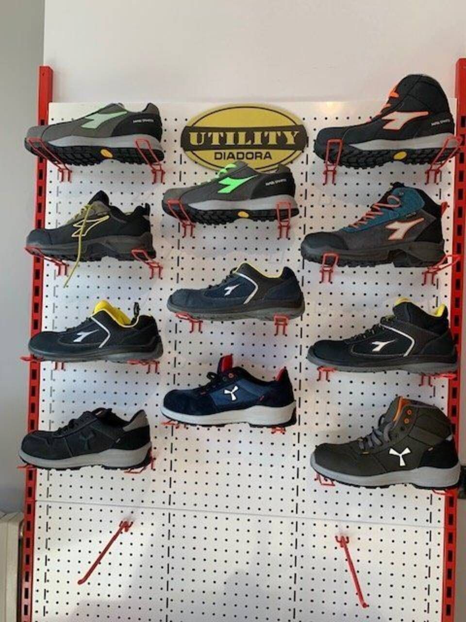 Esposizione di scarpe da lavoro Diadora Utility su un pannello forato, con vari stili e colori.