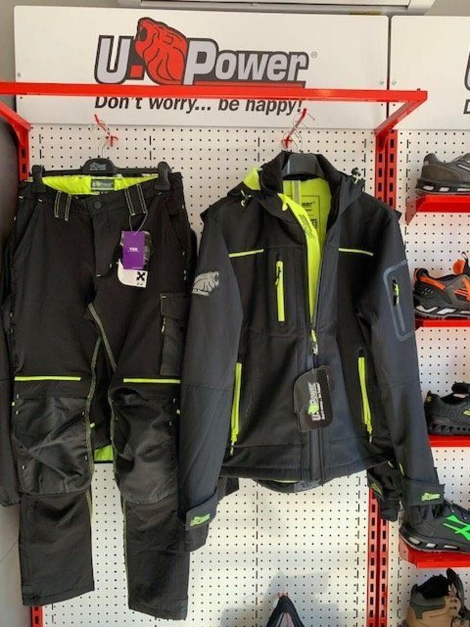 Pantaloni da lavoro e giacca neri e giallo neon appesi su un espositore con il logo U-Power.