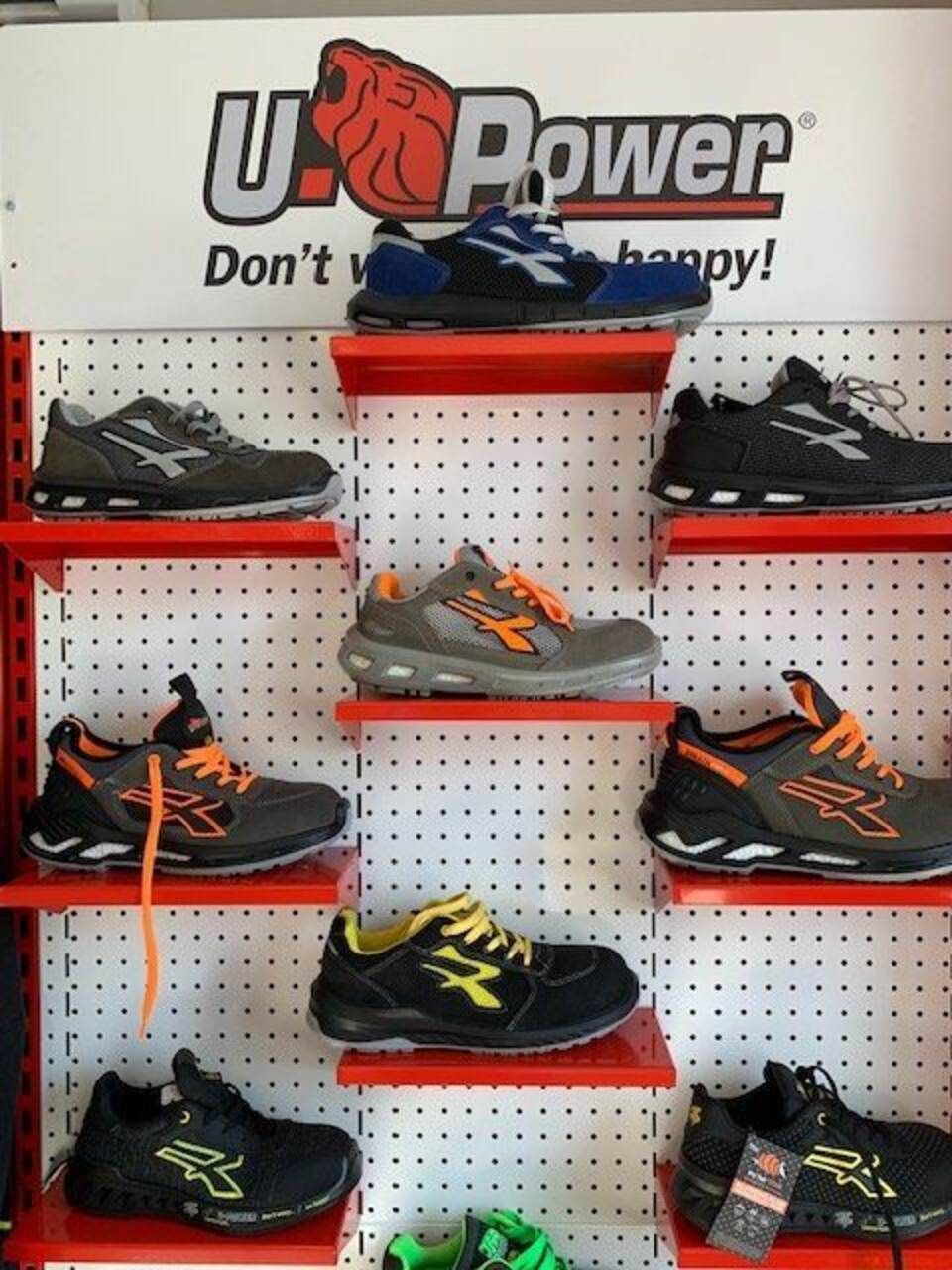 Scarpe esposte su scaffali rossi contro un pannello forato bianco, con il logo