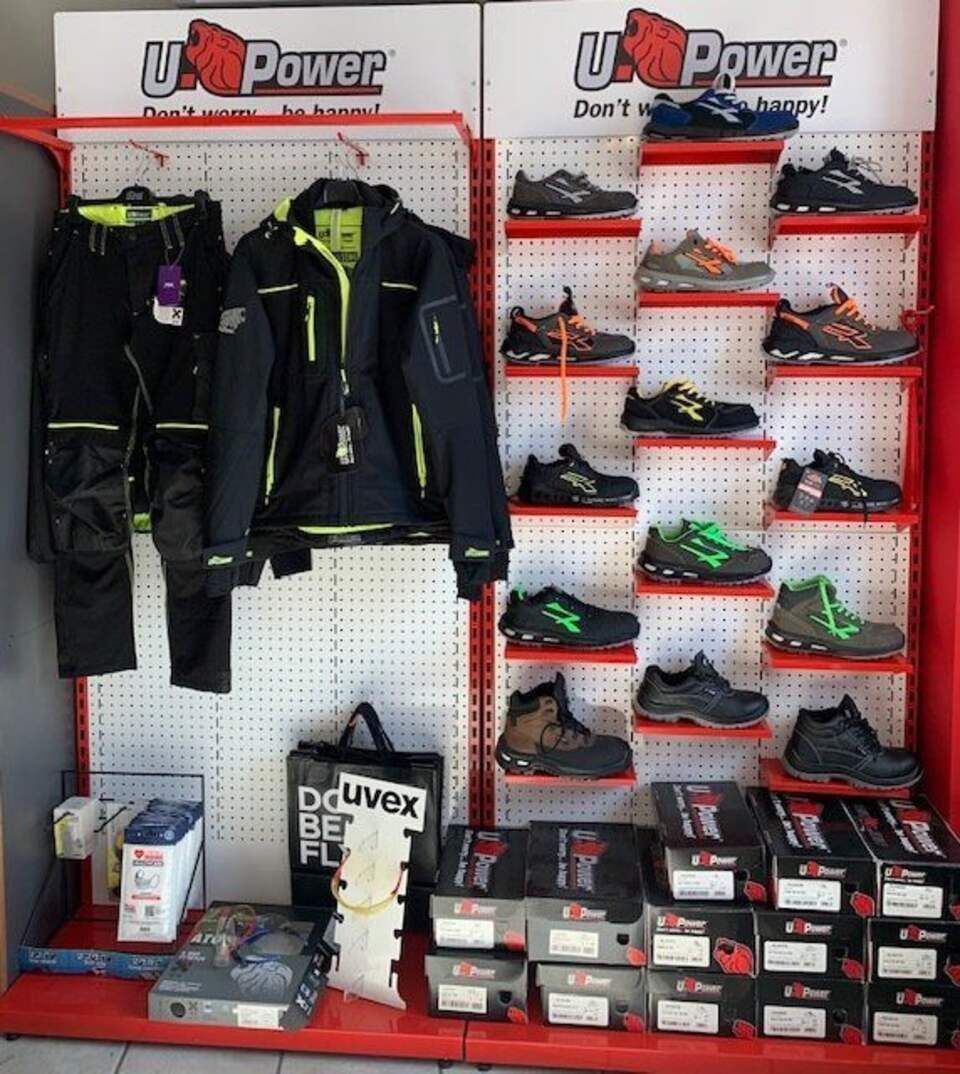 Esposizione di abbigliamento da lavoro e scarpe antinfortunistiche U-Power sullo scaffale di un negozio, con modelli di abbigliamento e scarpe in vari colori.