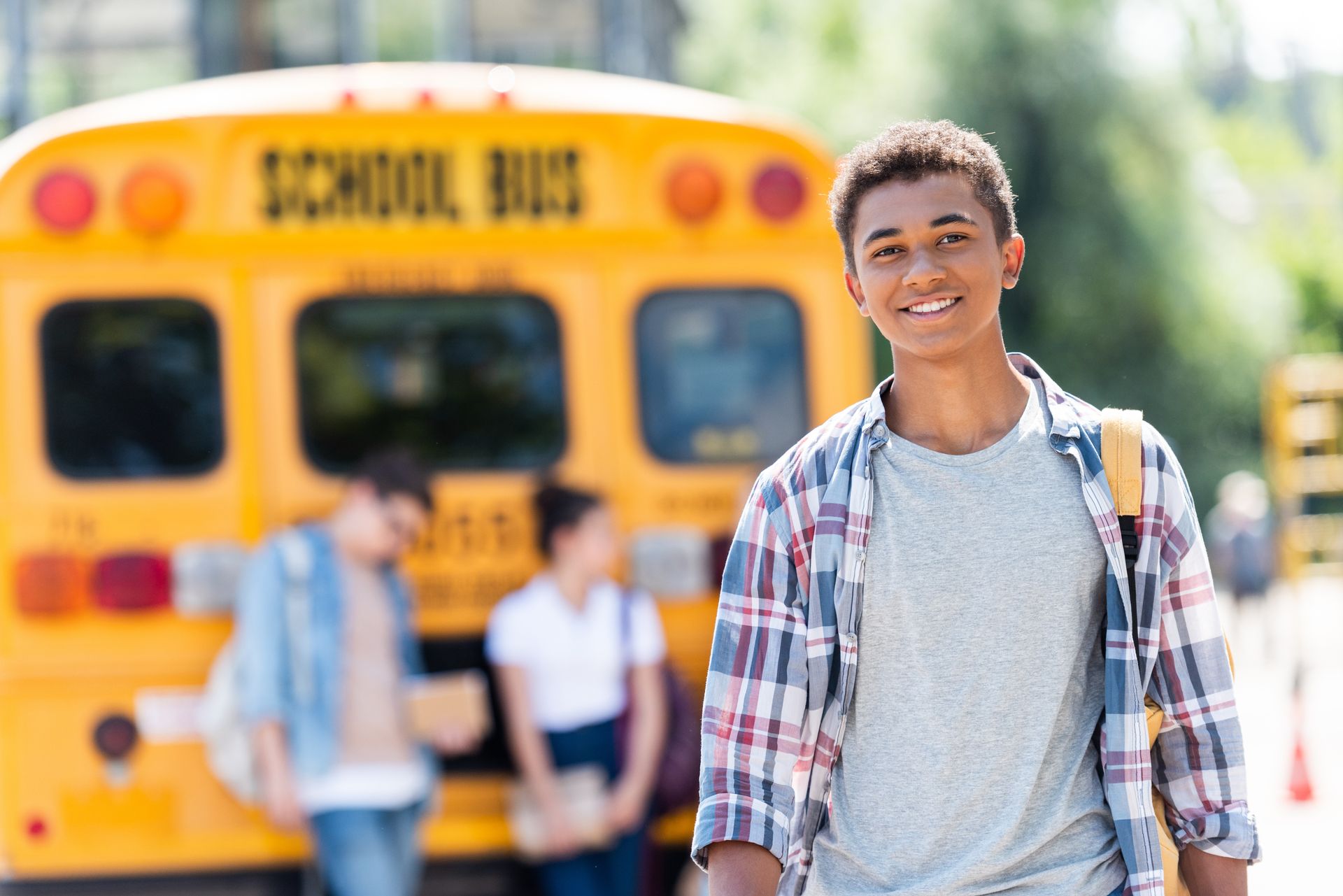 Schoolboy looking at camera in front of school bus.