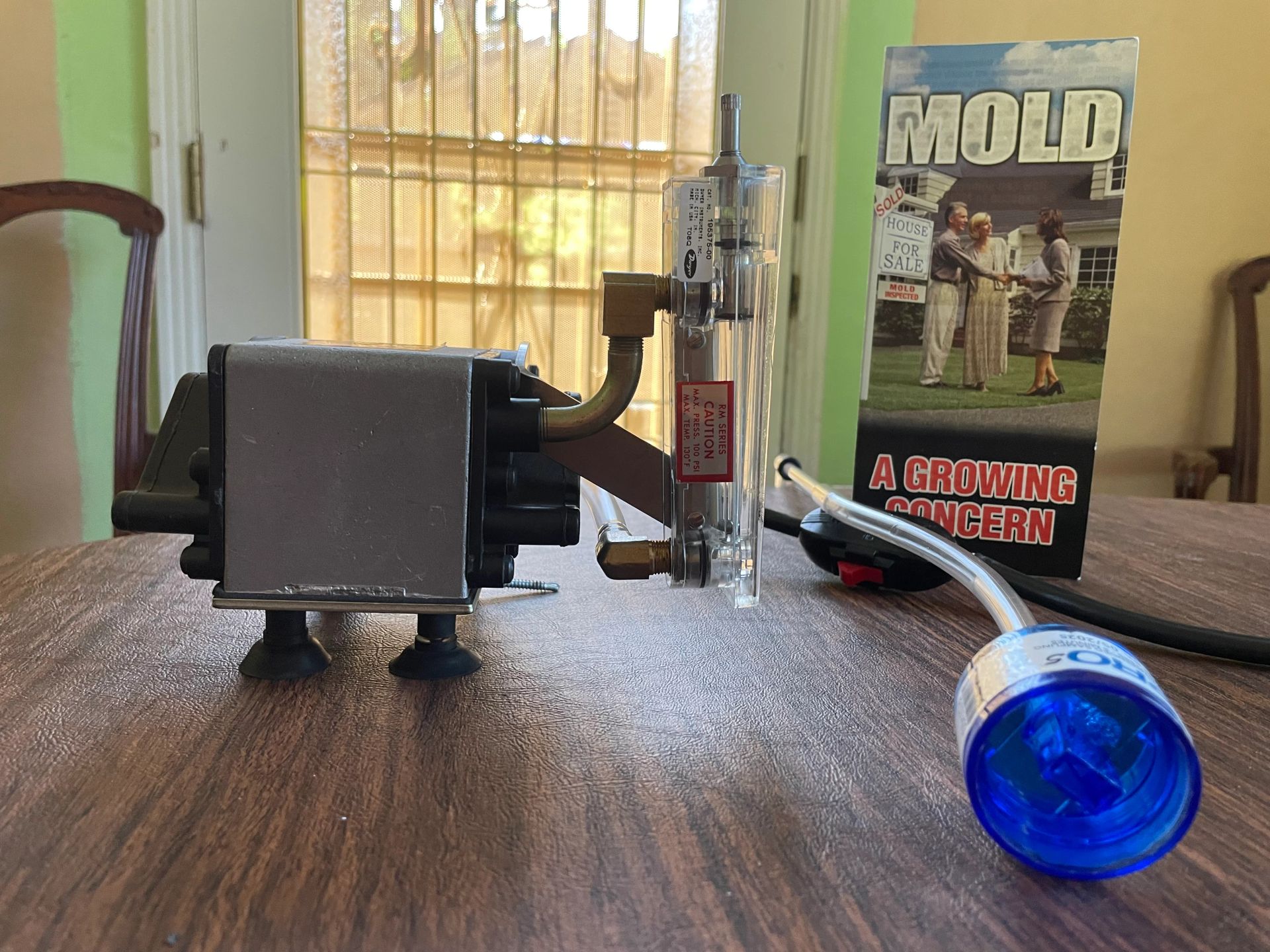 A Ghostbusters prop sits on a wooden table. Includes a box, a tube, and a blue light.