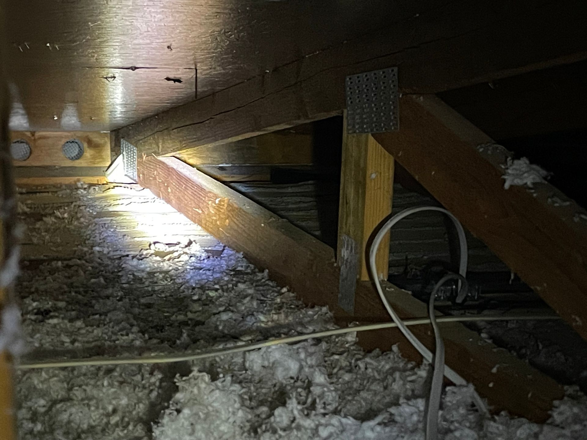 Inside an attic; wooden beams with insulation and wiring visible.