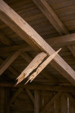Damaged wooden beam in the interior of a barn, with a large split and exposed wood fibers.