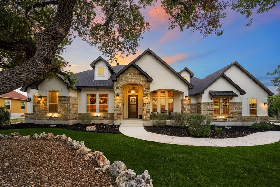 Single-story house with stone accents and illuminated windows; green lawn, dusk sky.