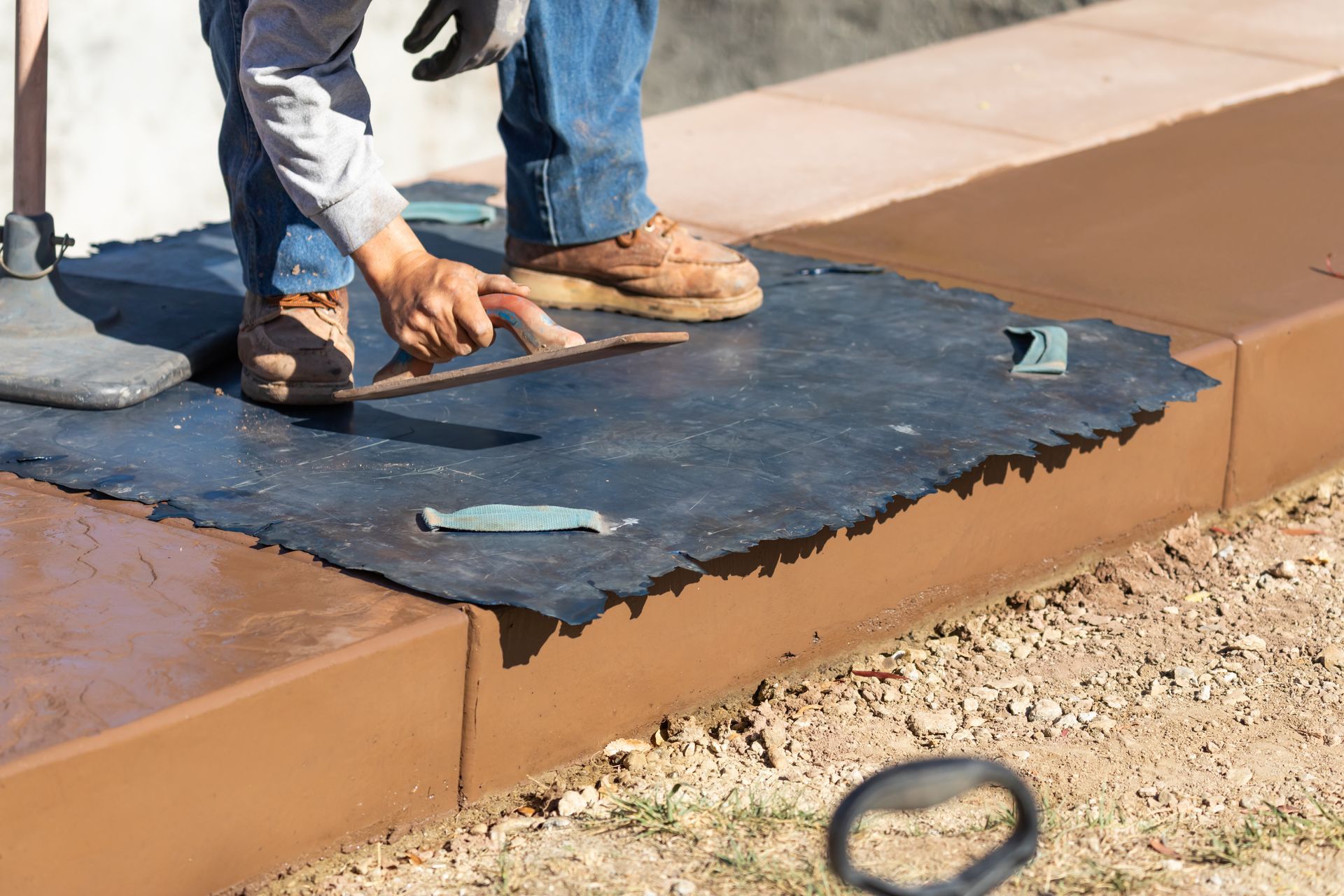 A man is laying concrete on a sidewalk with a trowel.