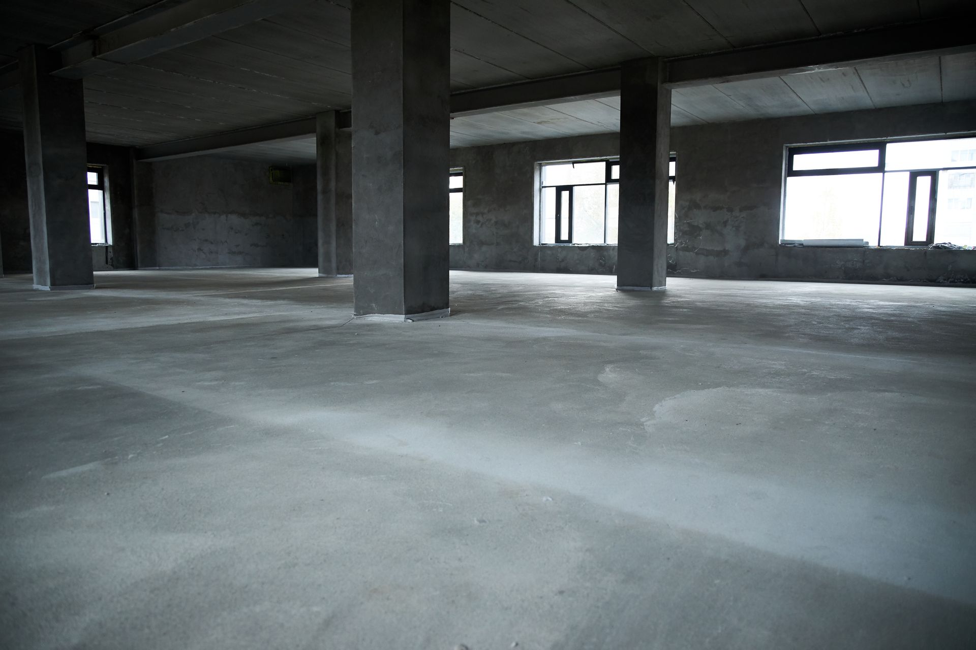 A large empty room with concrete floors and columns in a building under construction.