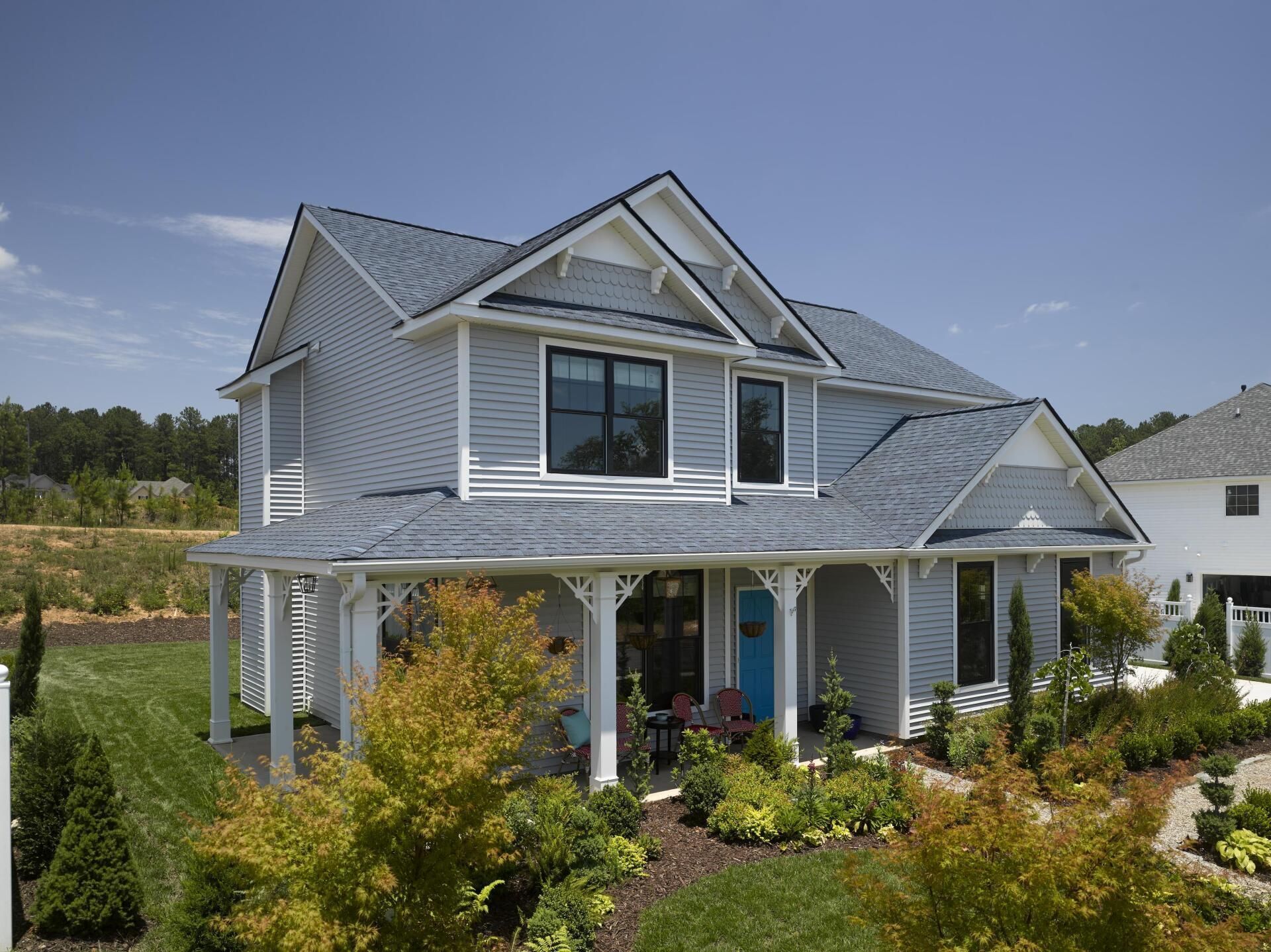 Two-story blue house with a white porch, blue door, and a landscaped front yard under a blue sky.