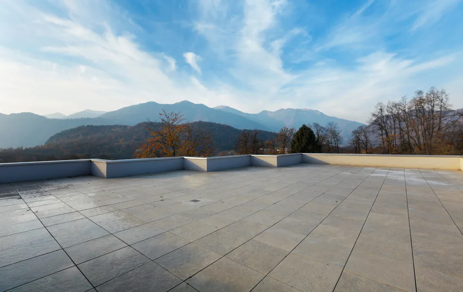 A large, tiled patio overlooks a mountain range under a partly cloudy, blue sky.