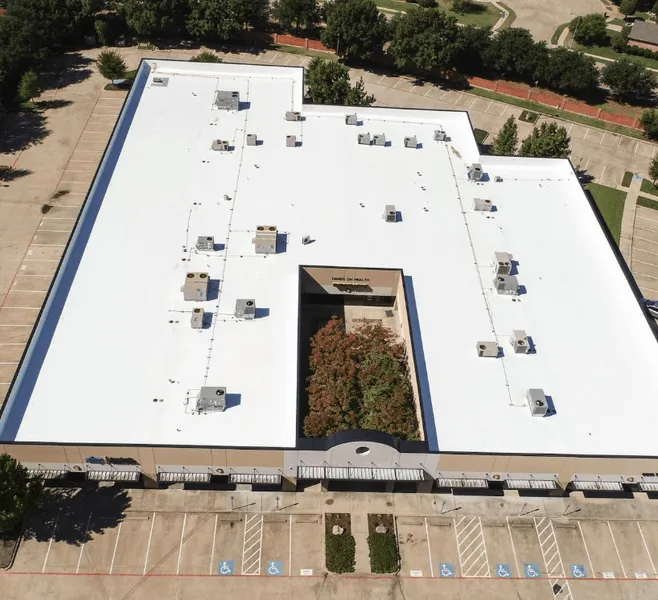 Aerial view of a commercial building with a white roof and multiple HVAC units; parking lot in the foreground.