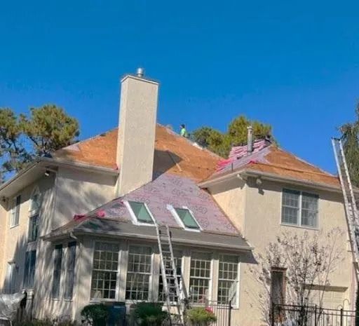 Roofers working on a beige house's roof, partial roof exposed, ladder present, clear blue sky.