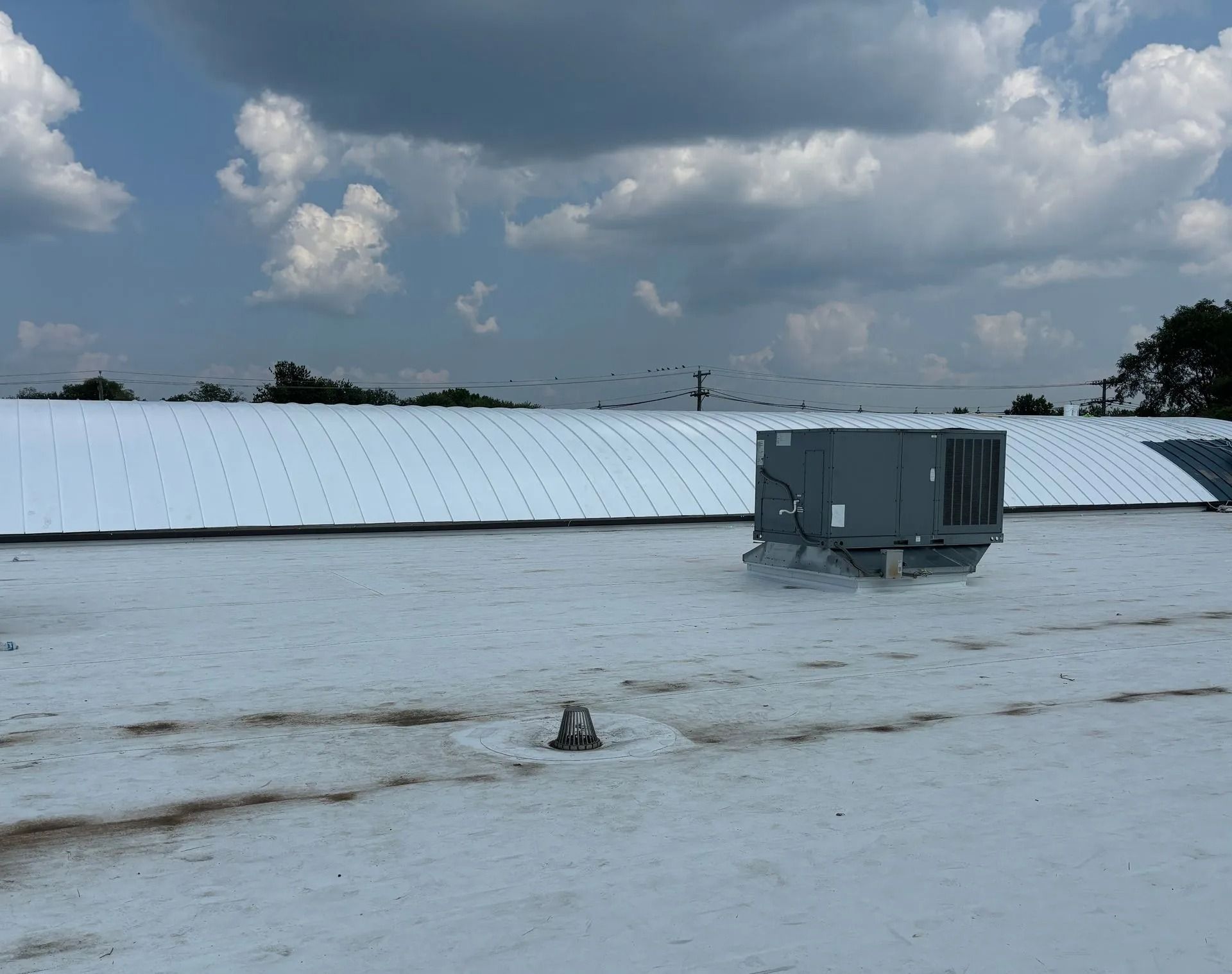Gray HVAC unit on white commercial roof under a cloudy sky.