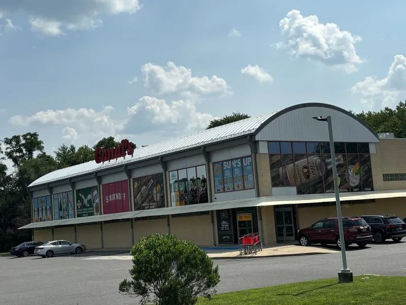 Exterior view of a store building with a curved roof. Cars are parked in front under a blue sky.