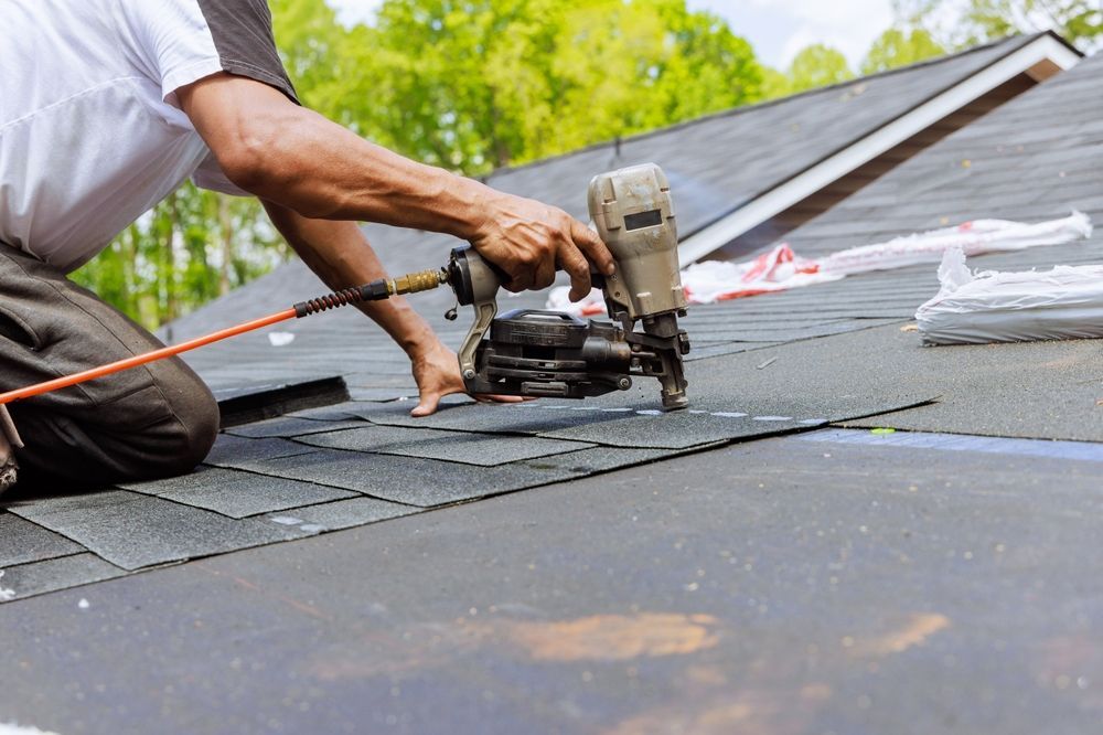 Roofer using a nail gun to install asphalt shingles on a rooftop.