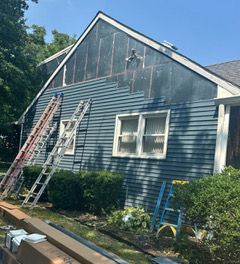 Two-story blue house with a white porch, blue door, and a landscaped front yard under a blue sky.