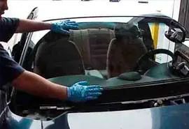 Persona con guantes azules instalando un parabrisas de coche.