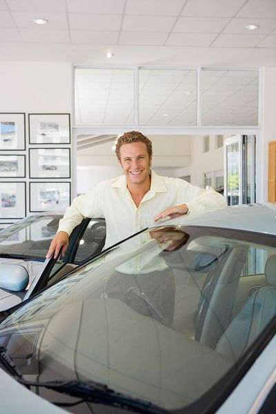 Hombre apoyado en un coche en una sala de exposición, sonriendo.