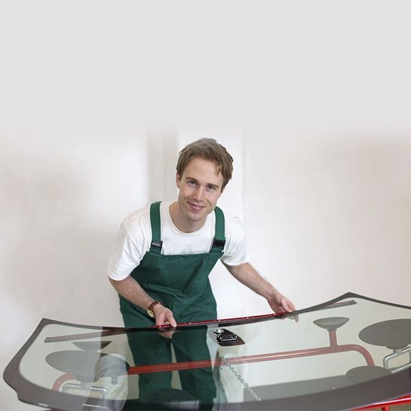 Mecánico con mono verde sosteniendo el parabrisas del coche, sonriendo.