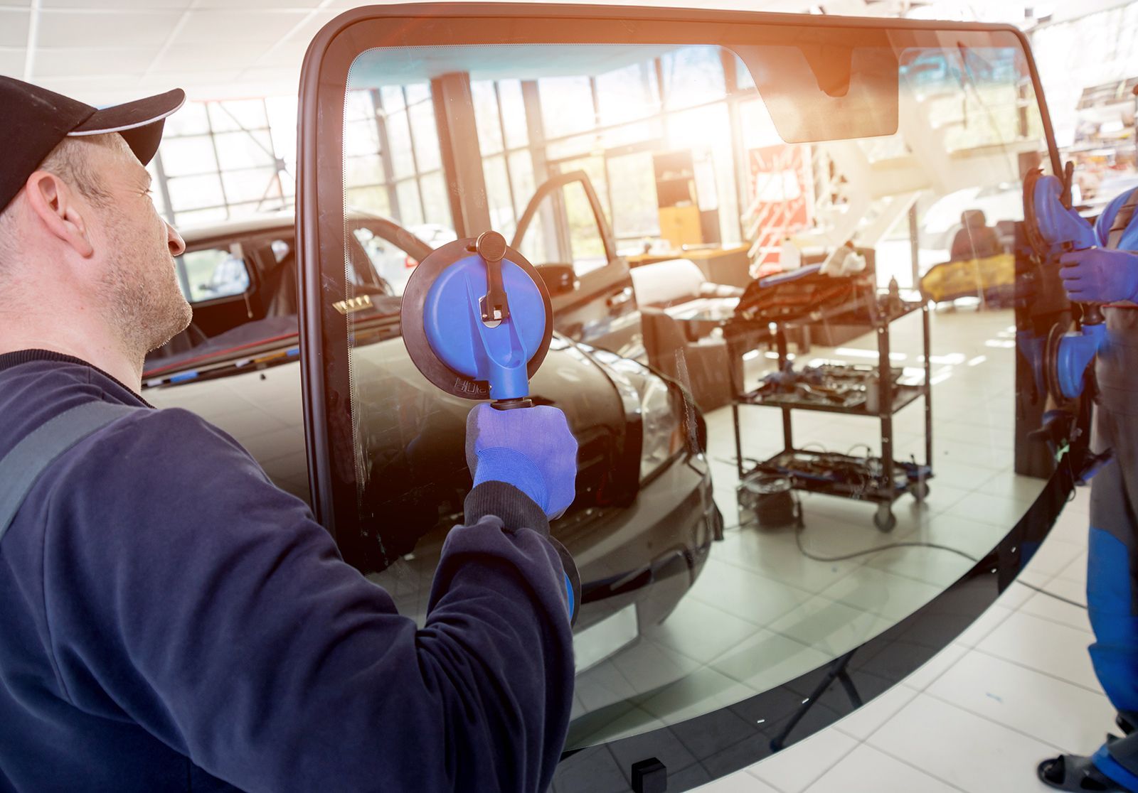 Dos personas instalando un parabrisas en un taller de reparación de automóviles; utilizando ventosas.