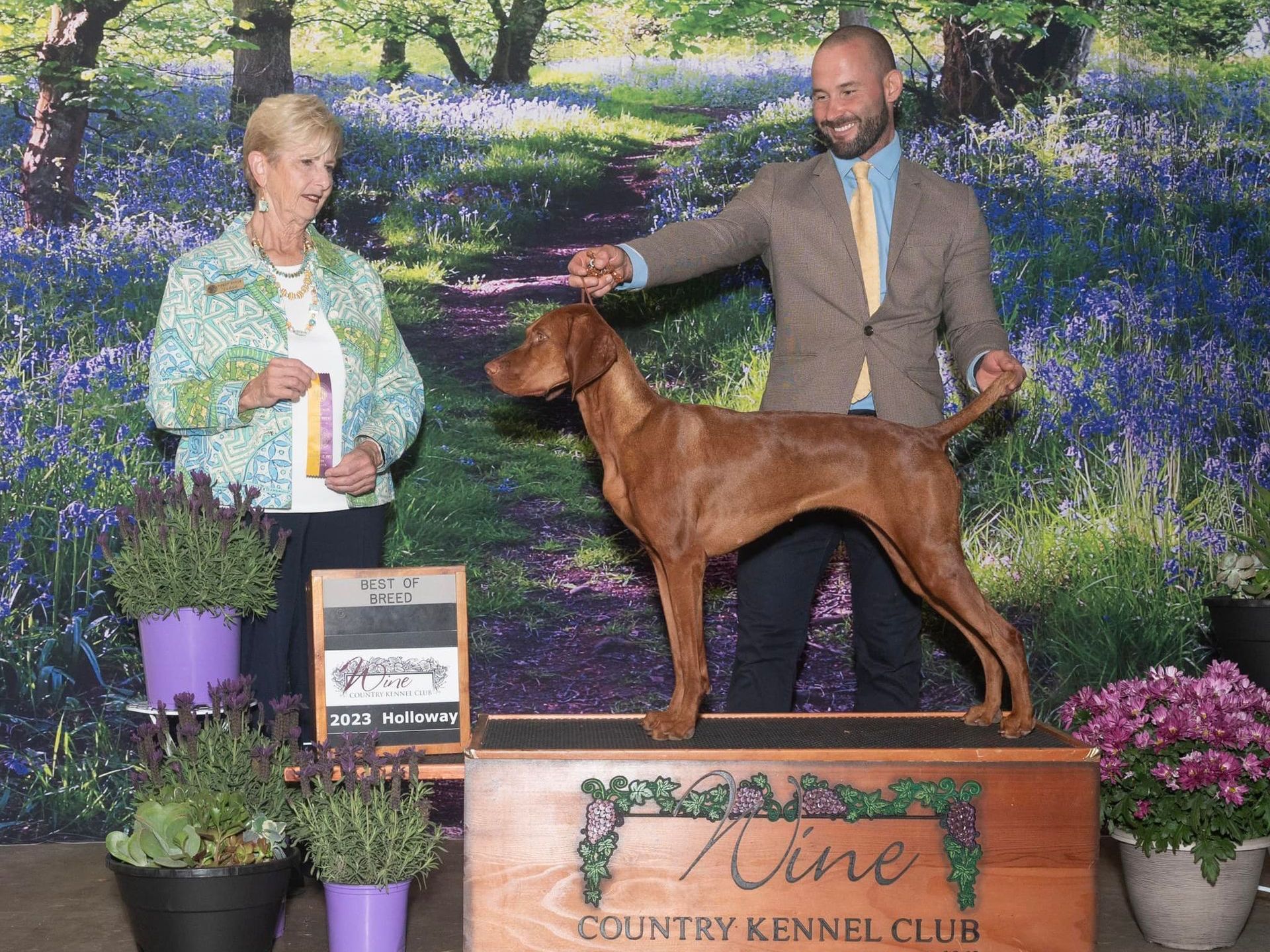 A man and woman are standing next to a brown dog.