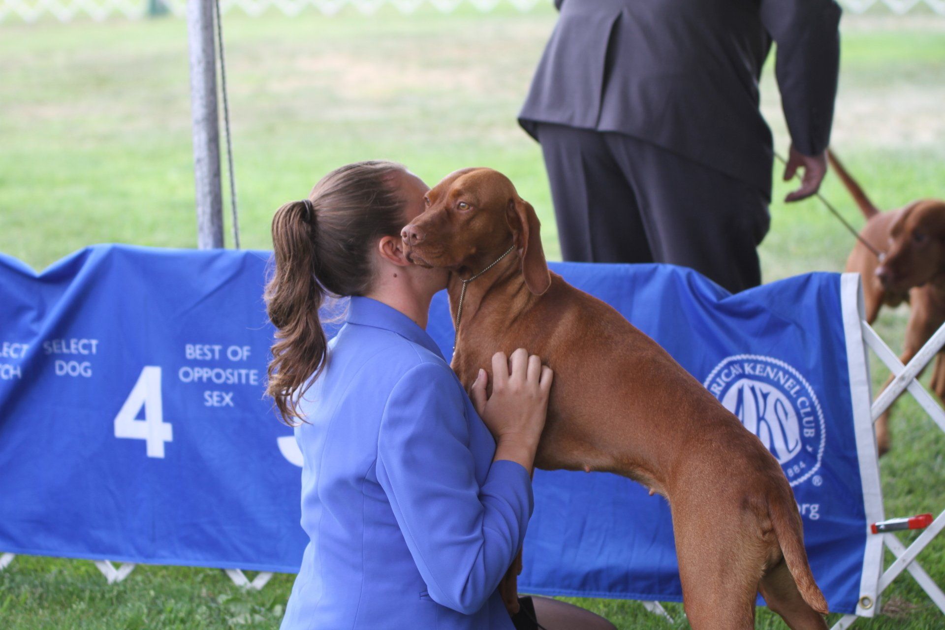 A woman kisses a brown dog at a dog show