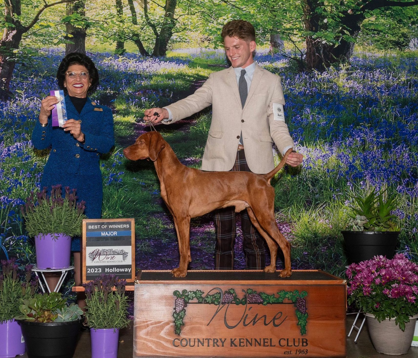 A man and woman standing next to a dog in front of a sign that says country kennel club