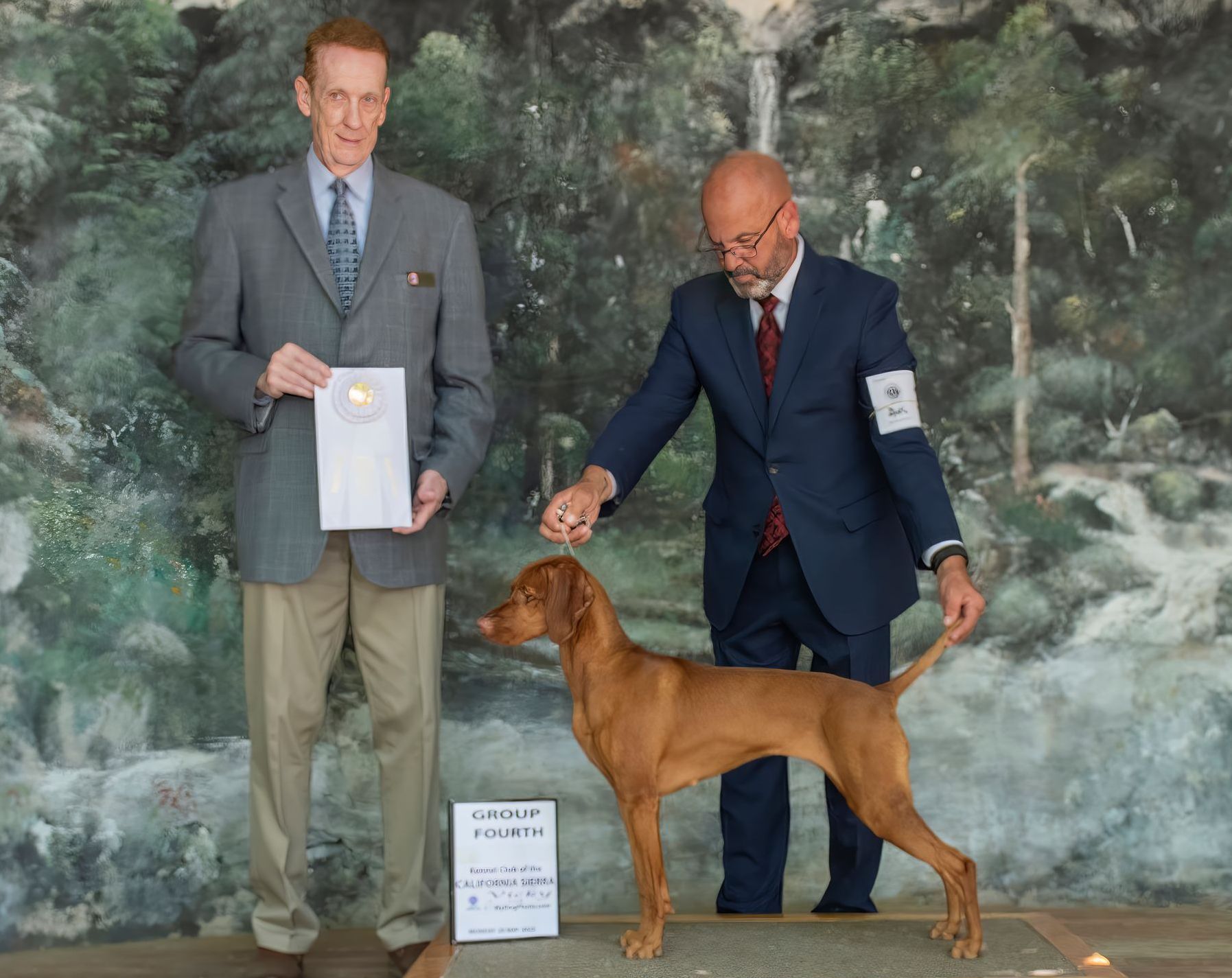 A man in a suit holds a certificate next to a dog