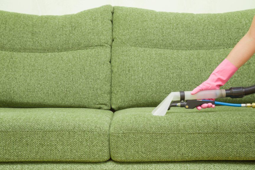 A Person in Pink Gloves Uses a Cleaning Tool on A Green Sofa — Les's Eco Carpet Cleaning in Byron Bay, NSW