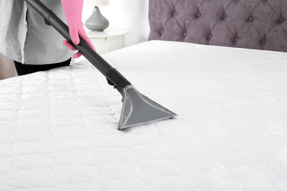 Person in Pink Gloves Vacuuming a White Mattress in A Bedroom — Les's Eco Carpet Cleaning in Byron Bay, NSW