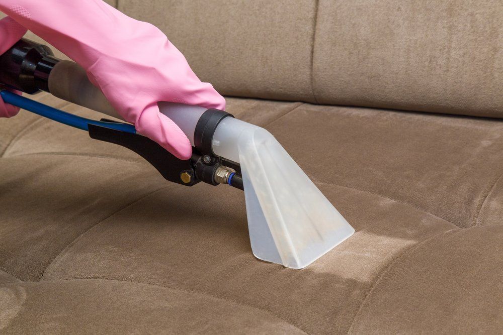 Person Using a Cleaning Tool on A Brown Upholstered Couch, Removing a Stain — Les's Eco Carpet Cleaning in Bangalow, NSW