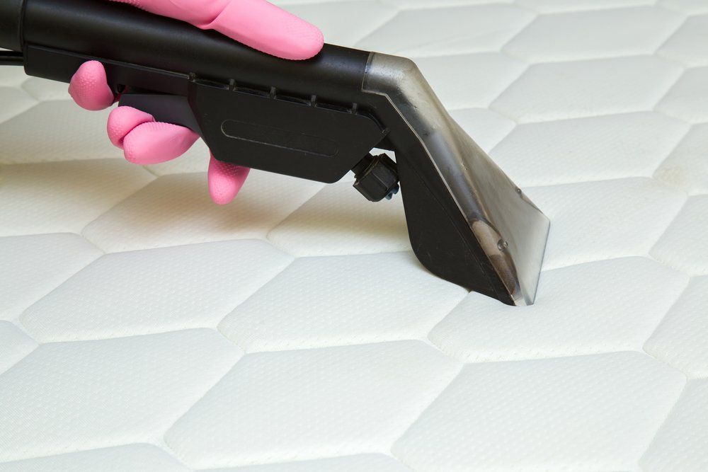Pink-Gloved Hand Using a Handheld Cleaner to Clean Quilted Mattress — Les's Eco Carpet Cleaning in Ocean Shores, NSW