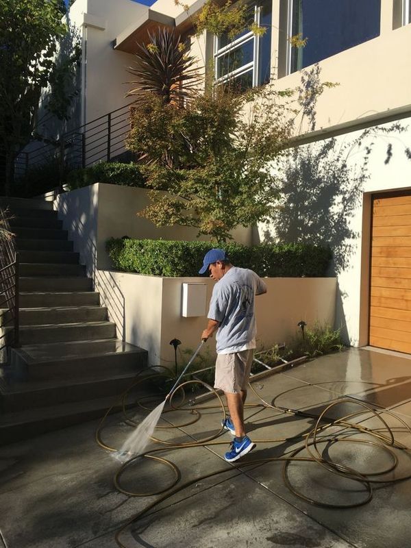 A man is using a pressure washer to clean a driveway in front of a house.