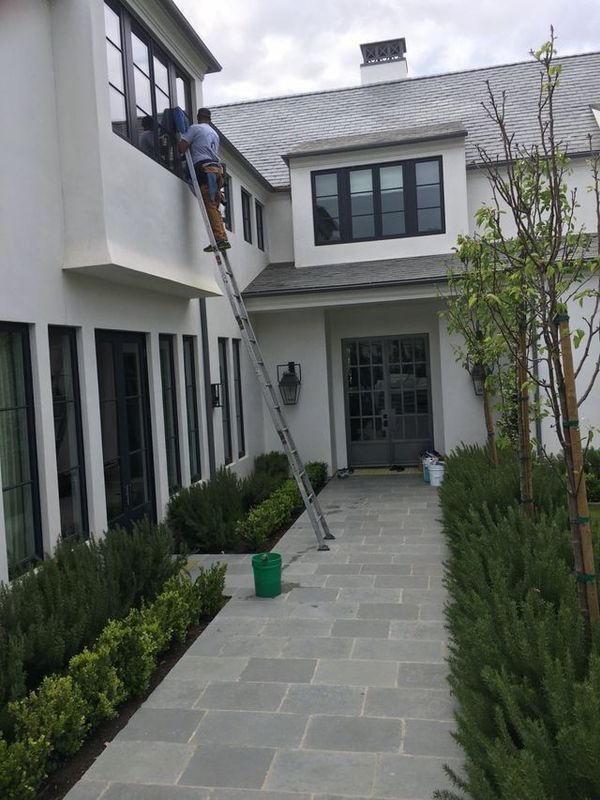 A man on a ladder is cleaning the windows of a large white house.