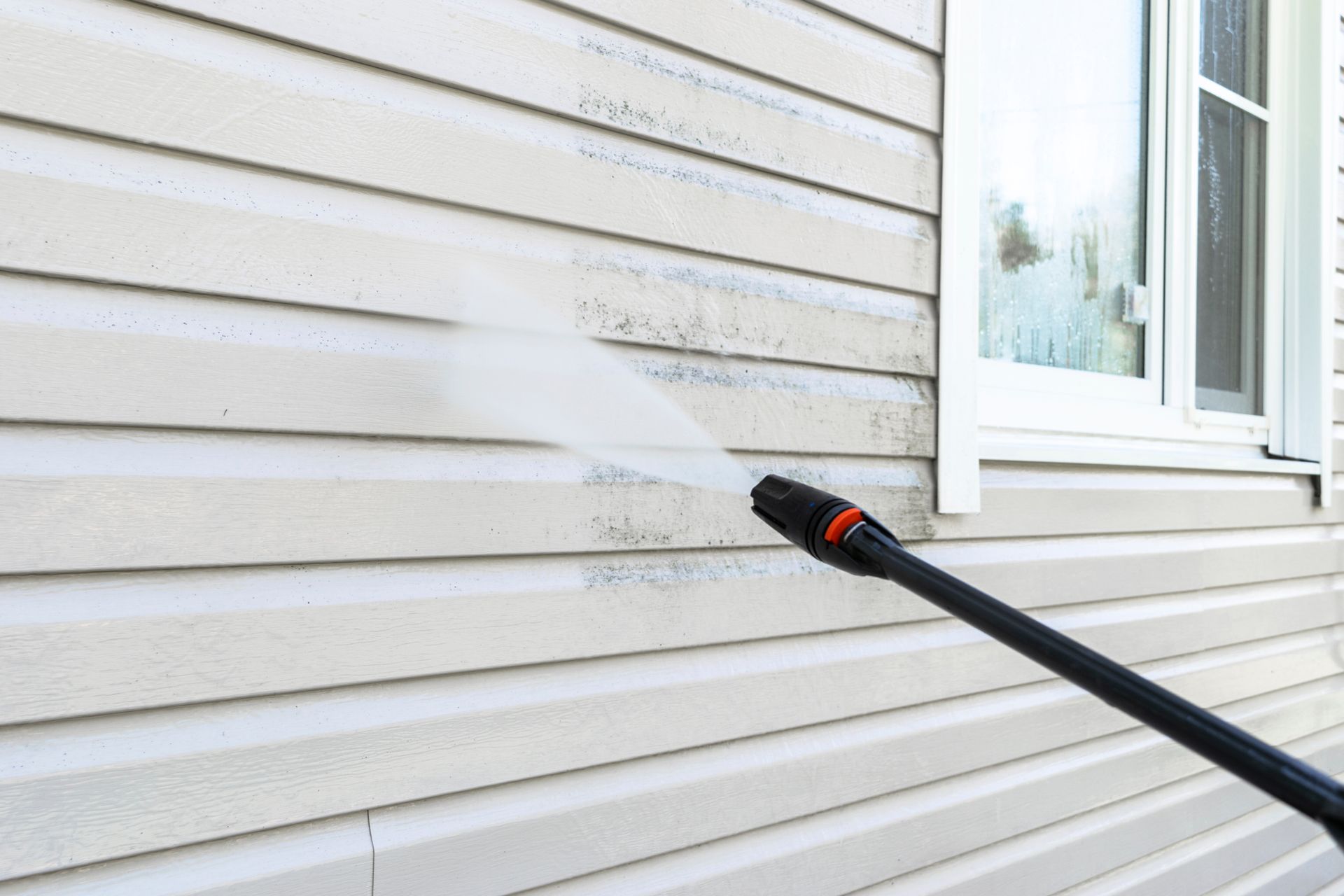 A person is cleaning the side of a house with a high pressure washer