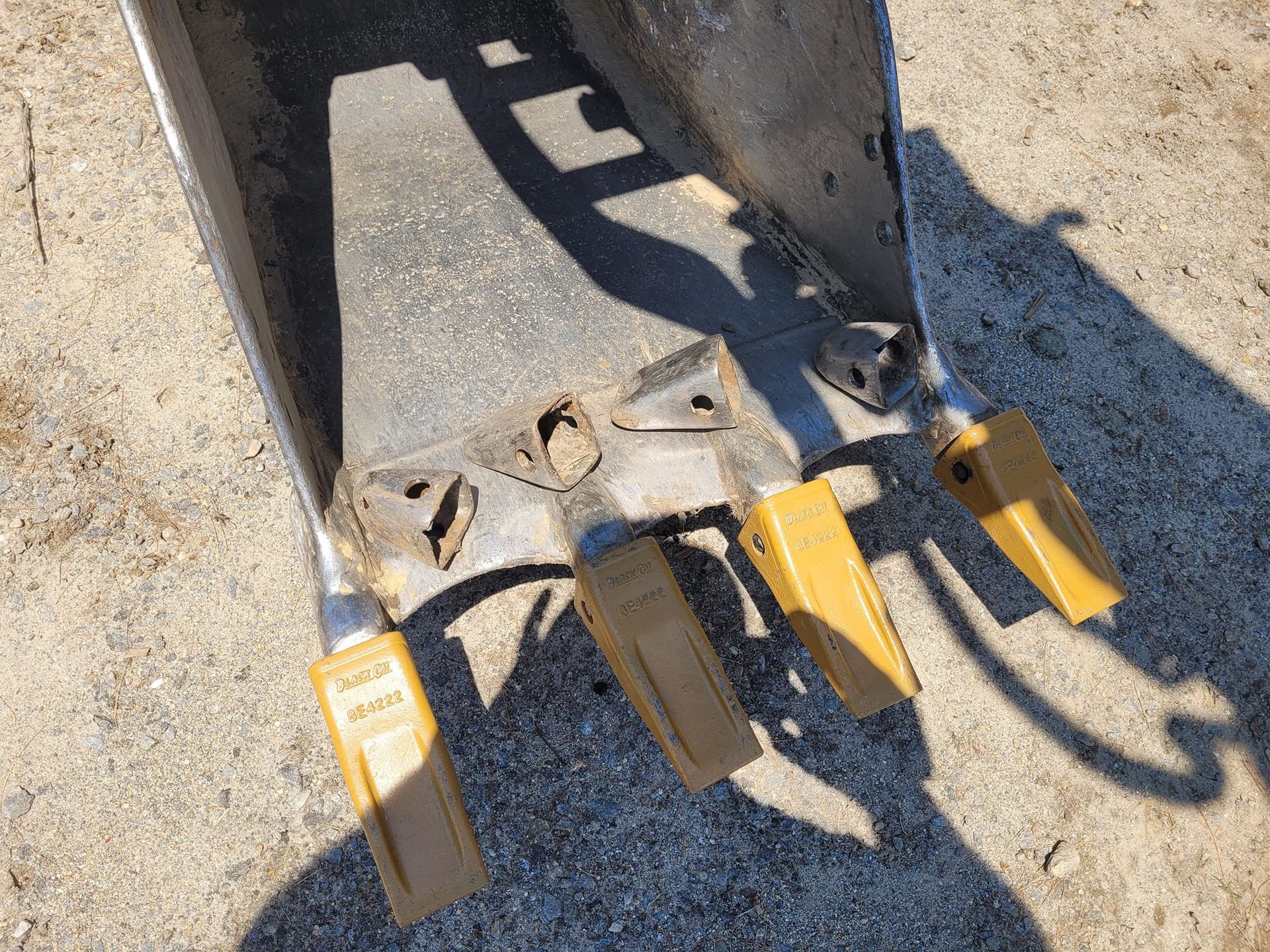 A close up of a shovel with a shadow on the ground.
