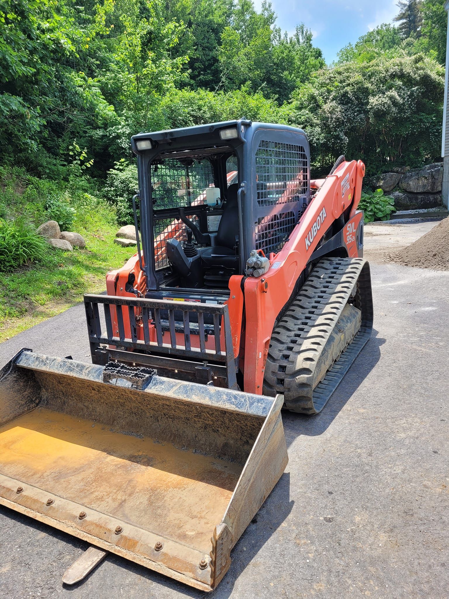 A red and black skid steer loader is parked on the side of the road.