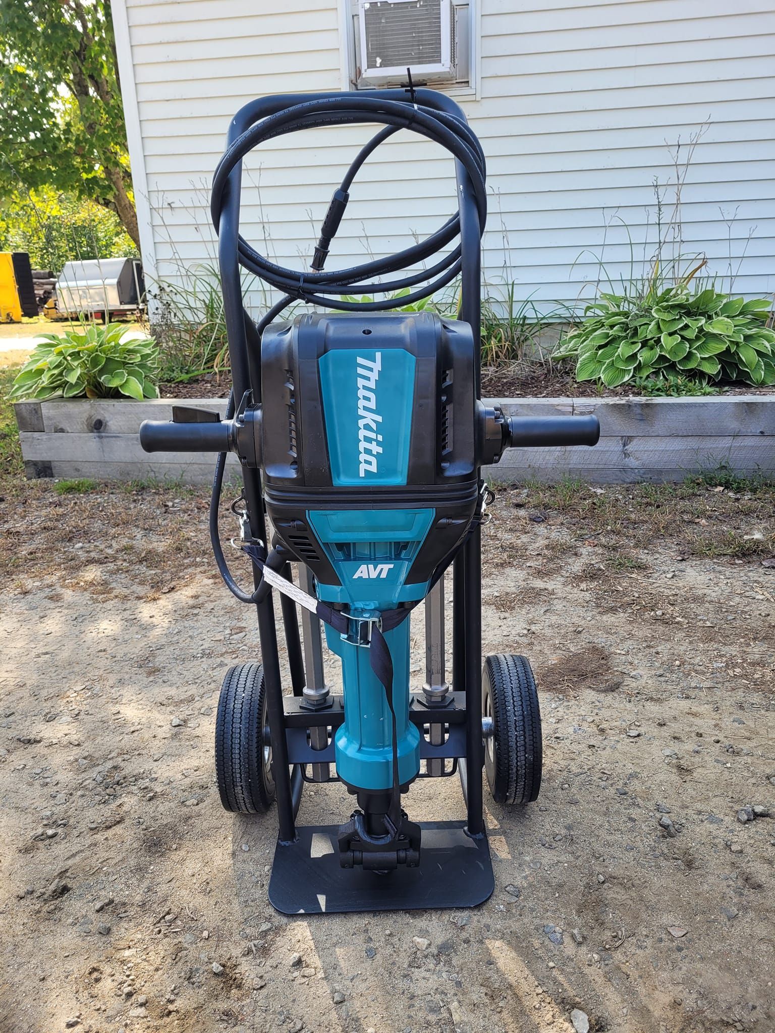 A makita demolition hammer is sitting on a cart in front of a house.