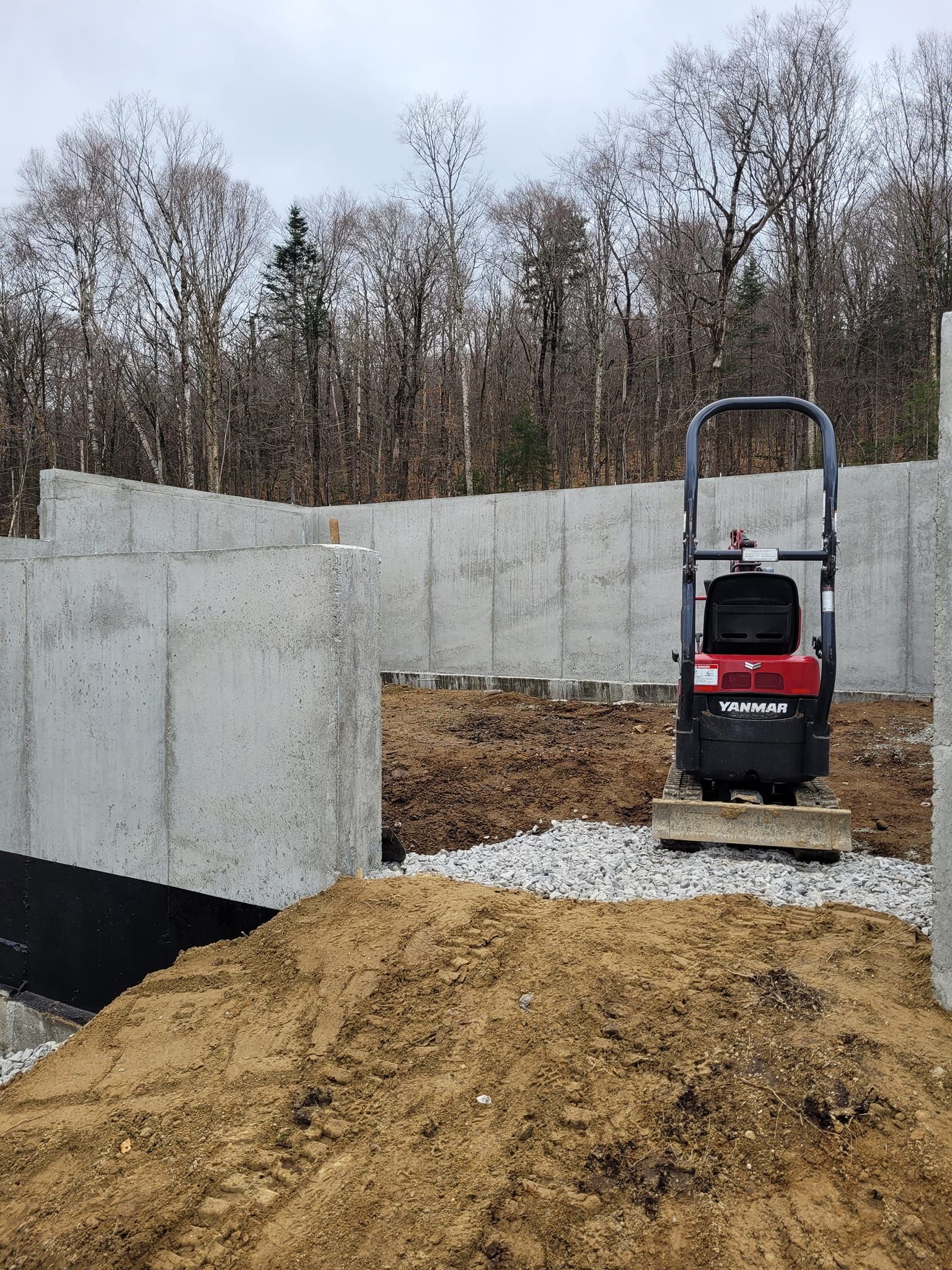 A small excavator is sitting on top of a pile of dirt in front of a concrete wall.