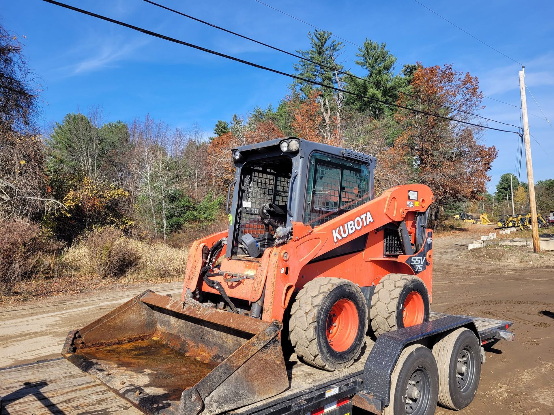 A bulldozer is sitting on top of a trailer on a dirt road.