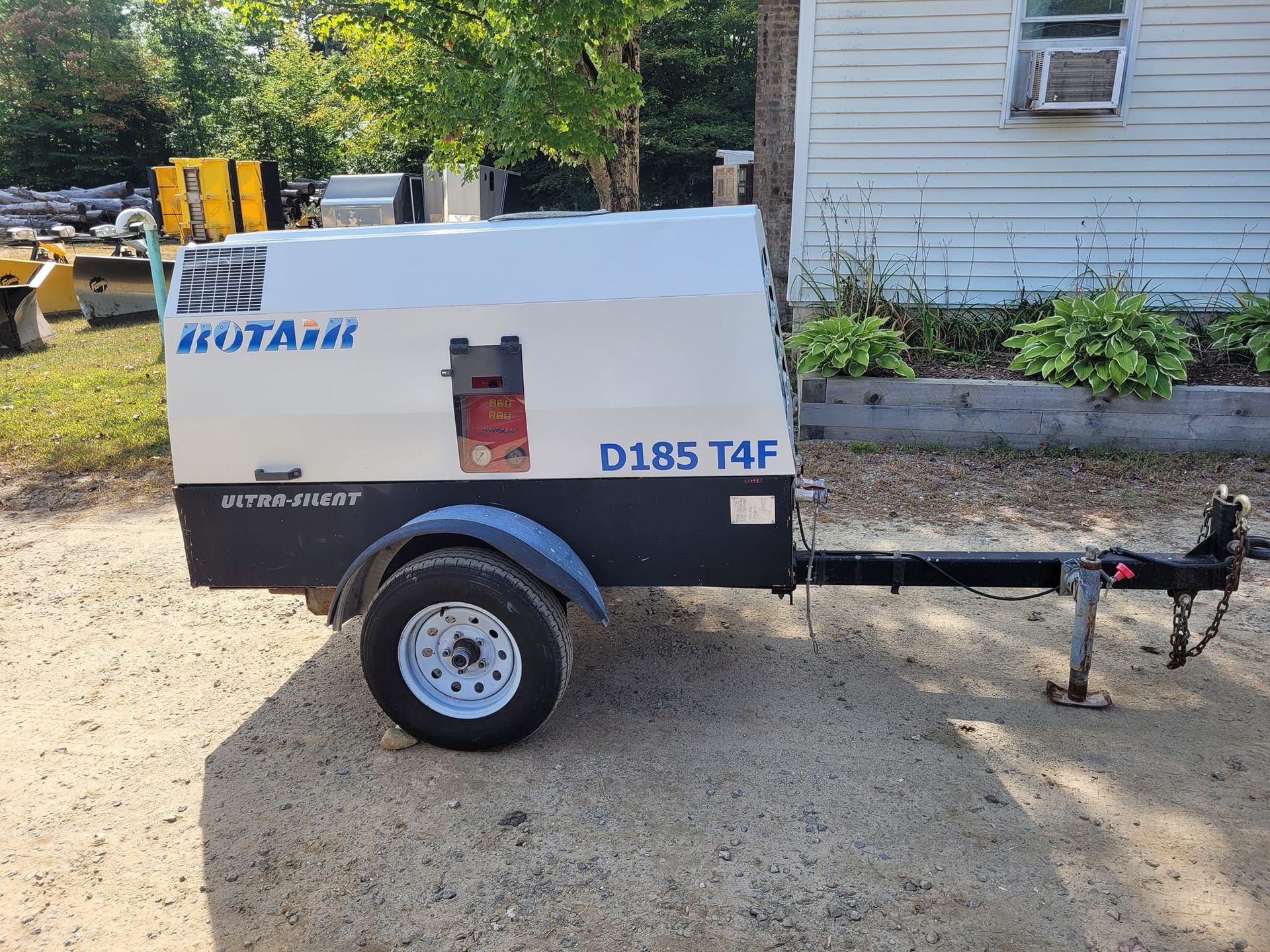 A rotary d185 t4f air compressor on a trailer is parked in front of a house.