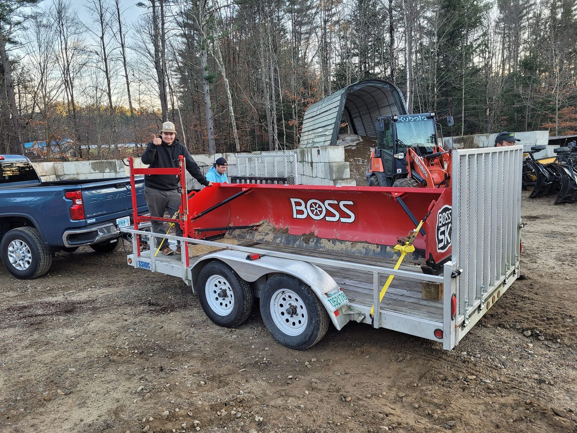 A man is standing next to a trailer with a tractor on it.
