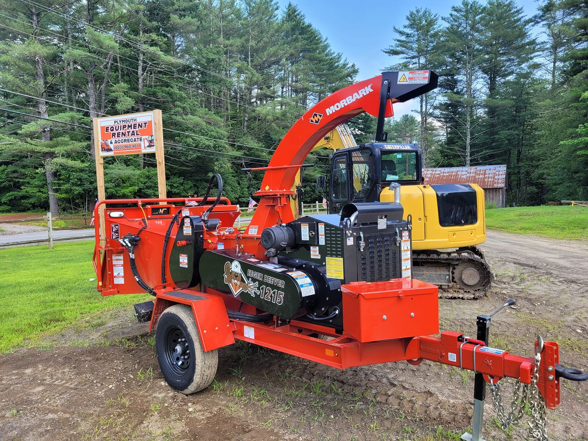 A red tree chipper is parked on a trailer next to a yellow excavator.