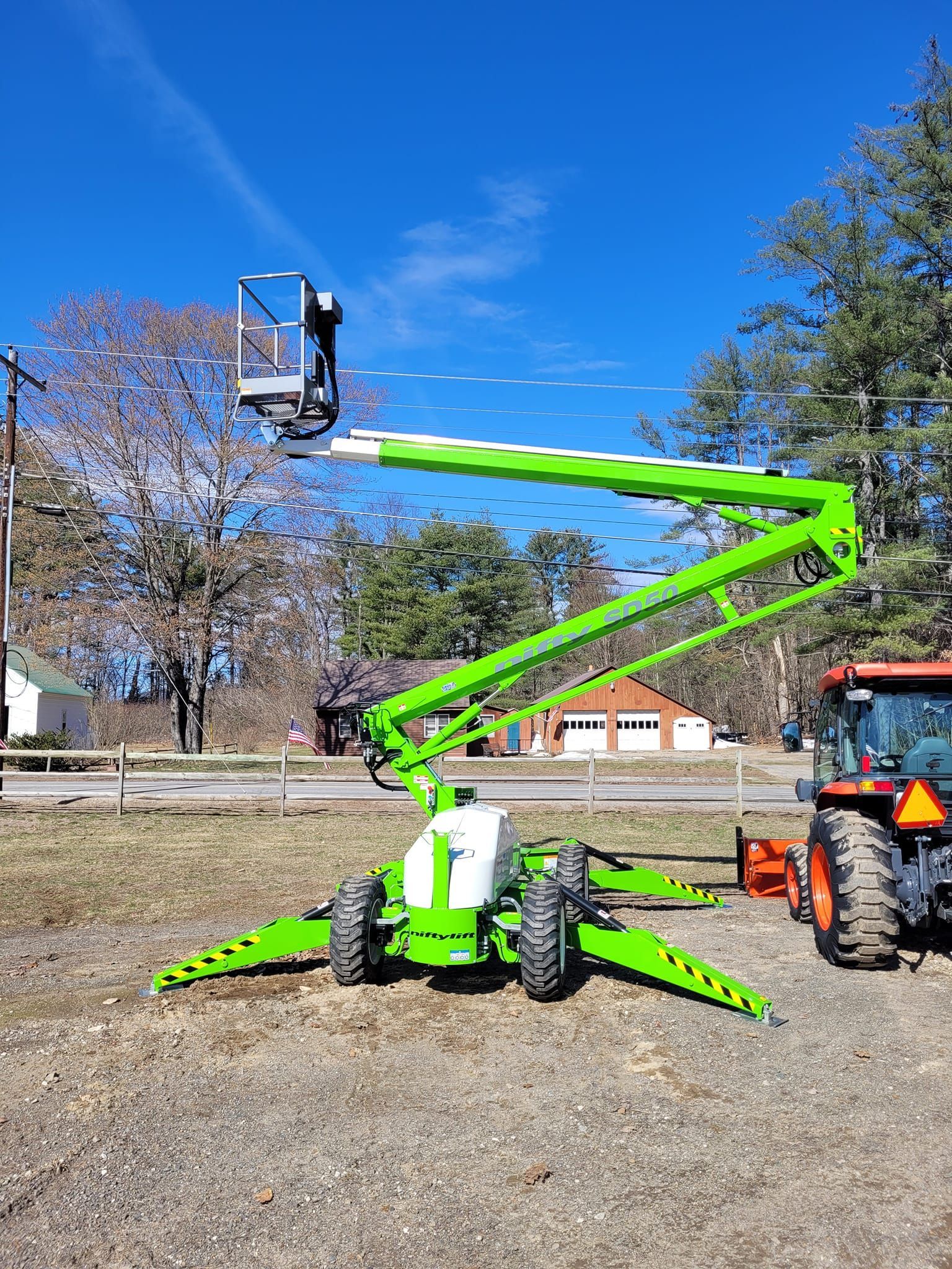 A green aerial lift is parked next to a tractor in a field.